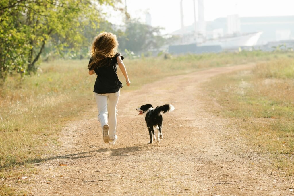 A woman jogging with her dog along a sunny path in a park, showcasing outdoor fitness and companionship.